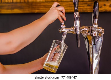 Close up of a barman hand at beer tap pouring a draught lager beer serving in a restaurant or pub, in a blurred background
