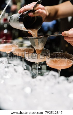 close up bartender hands, which makes and pours cocktail from shaker through a strainer into glass