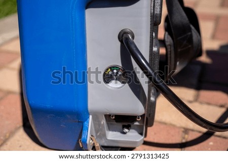 Close up of battery charge indicator voltmeter and control panel on an electric knapsack sprayer, showing technical details of gardening equipment.