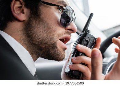 Close Up Of Bearded Bodyguard In Sunglasses Using Walkie Talkie In Car