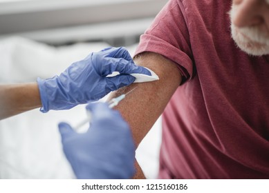 Close Up Of Bearded Old Man Receiving Vaccine Shot In Hand. Gentleman Sitting On Hospital Bed