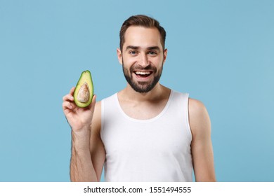 Close Up Bearded Young Man 20s Years Old In White Shirt Hold Half Of Avocado Isolated On Blue Pastel Background, Studio Portrait. Skin Care Healthcare Cosmetic Procedures Concept. Mock Up Copy Space