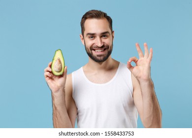 Close Up Bearded Young Man 20s Years Old In White Shirt Hold Half Of Avocado Isolated On Blue Pastel Background, Studio Portrait. Skin Care Healthcare Cosmetic Procedures Concept. Mock Up Copy Space