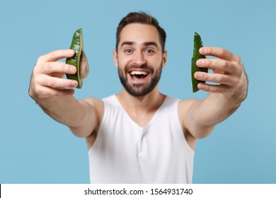 Close Up Bearded Young Man 20s Years Old In White Shirt Hold Half Of Avocado Isolated On Blue Pastel Background, Studio Portrait. Skin Care Healthcare Cosmetic Procedures Concept. Mock Up Copy Space