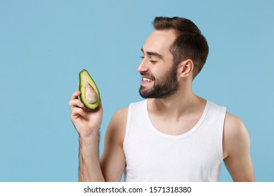 Close Up Bearded Young Man 20s Years Old In White Shirt Hold Half Of Avocado Isolated On Blue Pastel Background, Studio Portrait. Skin Care Healthcare Cosmetic Procedures Concept. Mock Up Copy Space