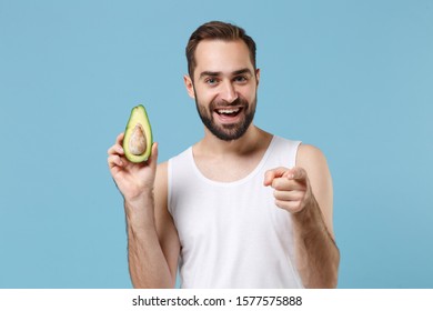 Close Up Bearded Young Man 20s Years Old In White Shirt Hold Half Of Avocado Isolated On Blue Pastel Background, Studio Portrait. Skin Care Healthcare Cosmetic Procedures Concept. Mock Up Copy Space