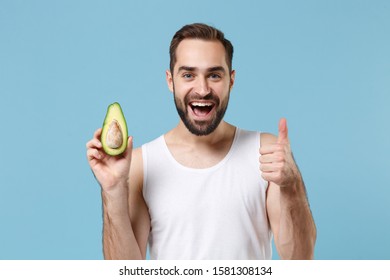 Close Up Bearded Young Man 20s Years Old In White Shirt Hold Half Of Avocado Isolated On Blue Pastel Background, Studio Portrait. Skin Care Healthcare Cosmetic Procedures Concept. Mock Up Copy Space