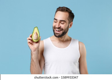 Close Up Bearded Young Man 20s Years Old In White Shirt Hold Half Of Avocado Isolated On Blue Pastel Background, Studio Portrait. Skin Care Healthcare Cosmetic Procedures Concept. Mock Up Copy Space