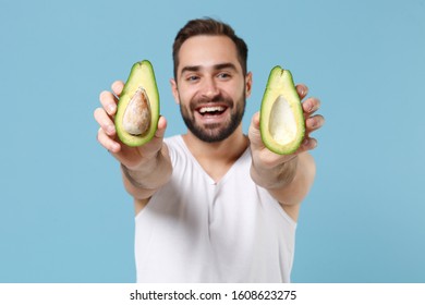 Close Up Bearded Young Man 20s Years Old In White Shirt Hold Half Of Avocado Isolated On Blue Pastel Background, Studio Portrait. Skin Care Healthcare Cosmetic Procedures Concept. Mock Up Copy Space