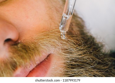 Close up of beautician applying gel serum on bearded man face using glass pipette