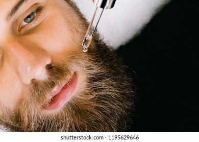 Close up of beautician applying gel serum on bearded man face using glass pipette