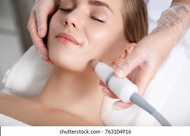 Close up of beautician hand making ultrasound facial procedure by special equipment. Her closed eyes with slight smile - Powered by Shutterstock