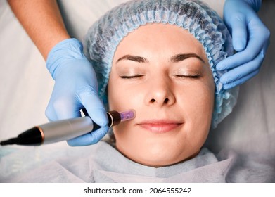 Close up of beautician hands in sterile gloves using dermapen during skincare procedure. Young woman receiving facial treatment in beauty salon. Concept of skincare and collagen induction therapy.