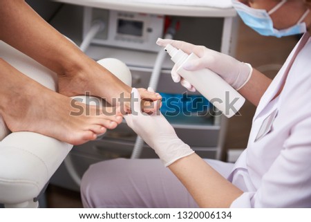 Close up of beautician hands in sterile gloves spraying lotion on lady feet before the procedure