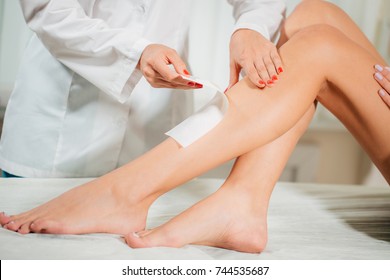 Close Up Beautician Waxing A Womans Leg Applying A Strip Of Material Over The Hot Wax Close Up Beautician Waxing A Womans Leg Applying A Strip Of Material Over The Hot Wax