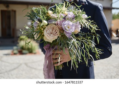Close up of beautiful bridal bouquet of pink and purple flowers and greenery in groom's hand outdoors, copy space. Wedding concept