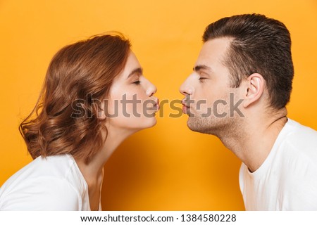 Close up of a beautiful couple wearing white t-shirts standing isolated over yellow background, kissing