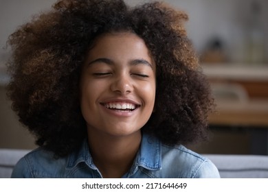 Close up beautiful face of African teenage girl closed her eyes deep in pleasant thoughts, feel happy, enjoy fresh pleasant fragrance sit on sofa at home. Natural beauty, dreams, visualization concept - Powered by Shutterstock