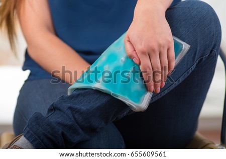 Close up of a beautiful female holding ice gel pack on leg, medical concept, in office background