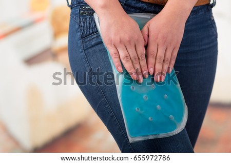 Close up of a beautiful female holding ice gel pack on leg, medical concept, in office background