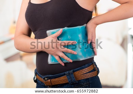 Close up of a beautiful female holding ice gel pack on her waist, medical concept, in office background