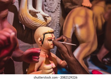 Close up of beautiful Kartik god idol face, also known as Kartikeya. Sculptor of a Hindu god. An artist doing fine detail work with a brush on eyes of Indian statue at a workshop.