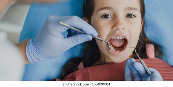 Close up of a beautiful little girl siting in a stomatology seat having a tooth examination by a pediatric stomatologist.