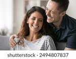 Close up beautiful overjoyed Latin couple talking, laughing, spend time together at home. Cheerful husband hugs his beloved beautiful wife, joking, giggling, feel carefree and happy. Relations, love