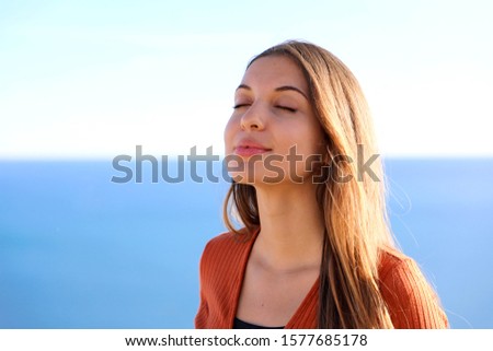 Close up of beautiful relaxed girl breathing and smiling with blue sea on the background.