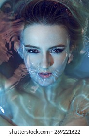 Close up of beautiful sexy young woman lying in the bathtub. With gorgeous make-up. Open mouth under water and sexy looking at camera. Blue and red lightning.