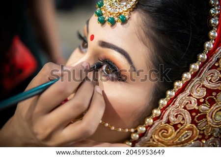 Close up of the beautiful traditional Indian bride getting ready for her wedding day. Cropped hand of makeup artist doing a makeup of bridal face and applying eyeliner.