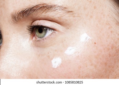 Close Up Of Beautiful Woman Face With Clean Fresh Skin And Points Of White Moisturizing Cream Under Eye. Concept Of Beauty Cleanliness Perfection And Skincare