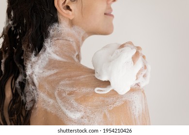 Close up beautiful woman taking shower with moisturizing soap, using fluffy soft puff, applying foamy lotion or soap on body skin, attractive young female enjoying morning routine procedure, spa