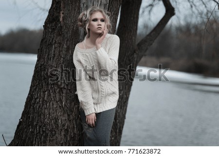 Close up of beautiful young  blonde woman with blue eyes in white pullover. 
Winter, spring, outdoor portrait. Professional beauty make-up: dark smoky eyes and pale lips and hair style.