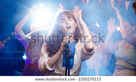 Close up of beautiful young caucasian woman singing song on a rooftop party. Friends enjoying rooftop party music, celebrating weekend reunion gathering.