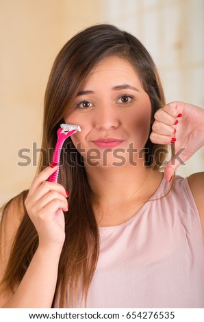 Close up of a beautiful young funny woman with an shaver on her face with a thumps down, in bath background