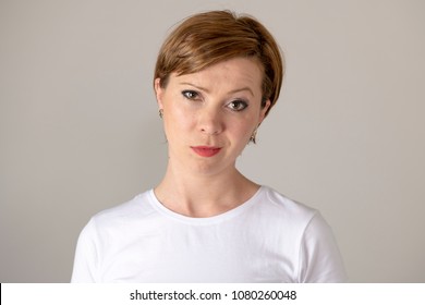 close up beautiful young red haired caucasian woman with a glaring face, half smiling showing concern. Human facial expressions and emotions. Gray background