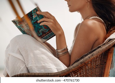 close up of beautiful young woman sitting in chair on beach and reading book