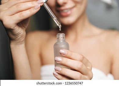 Close up of a beautiful young woman wrapped in towel applying cosmetic oil from a bottle on her face