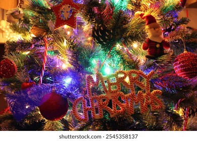 Close - up of a a beautifully decorated Christmas tree with Merry Christmas sign, red ornaments, candy cane, Santa Claus,  and glowing multi-colored lights – Festive holiday atmosphere - Powered by Shutterstock