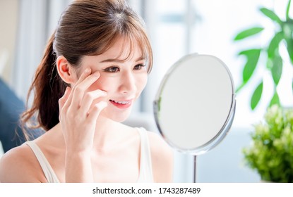 close up of beauty asian woman look her good skin near eyes in mirror at home