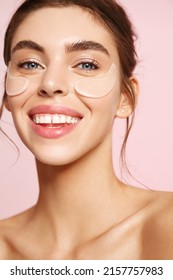Close up of beauty girl with natural no makeup look and white smile, has silicone under eye patches, smiling happy, using skincare products from dark circles and puffiness, pink background