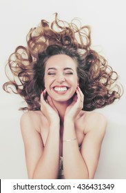 Close Up Beauty Portrait Of An Attractive Happy Young Laughing Woman Laying Down With Her Brunette Hair Curling Around Her, Joyfully Smiling With Perfect Teeth. Wellness Perfect Skin Lifestyle.
