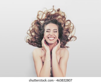 Close Up Beauty Portrait Of An Attractive Happy Young Laughing Woman Laying Down With Her Brunette Hair Curling Around Her, Joyfully Smiling With Perfect Teeth. Wellness Perfect Skin Lifestyle.