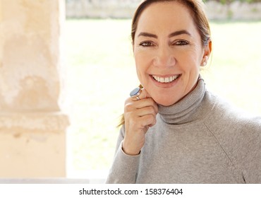 Close up beauty portrait of an attractive joyful and positive mature hispanic woman by a green grass garden during a sunny day at home, smiling and feeling positive.