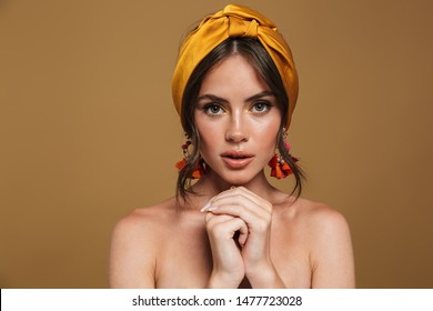Close up beauty portrait of an attractive young topless woman wearing headband standing isolated over brown background