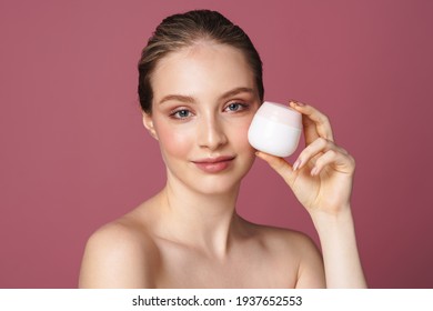 Close Up Beauty Portrait Of An Attractive Young Woman Showing Jar Of Face Cream Isolated Over Pink Background