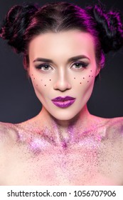 Close Up Beauty Portrait Of A Fantasy Art Theme. Two Buns Hairstyle With Purple Glitters And Stars All Over Woman Face And Body. Creative Violet Backlight, Studio Image