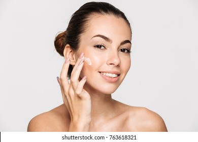 Close Up Beauty Portrait Of A Healthy Beautiful Half Naked Woman Applying Face Cream And Looking At Camera Isolated Over White Background