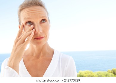 Close Up Beauty Portrait Of A Senior Mature Healthy Woman With Blue Eyes And Flawless Skin Crying And Drying Up Her Tears, Worried And Emotional. Mature And Aging Face With A Sad Expression, Outdoors.